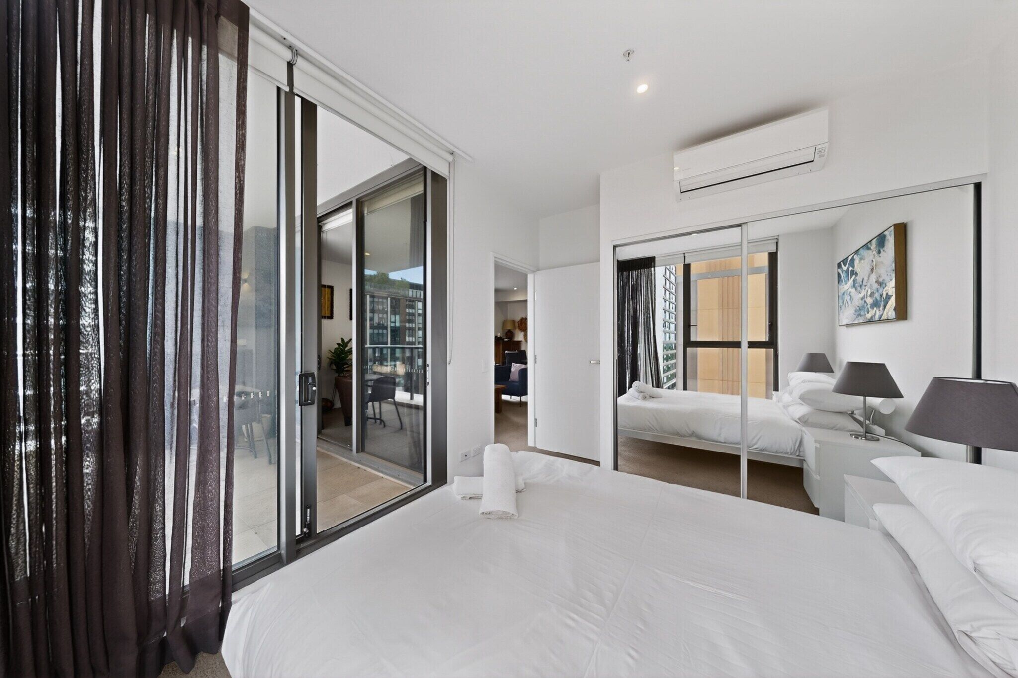 A hotel room with a large bed, a sliding glass door to a balcony, a small bedside table with a lamp, and a large mirror.