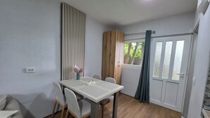 A dining area with a table, chairs, a vase with flowers, a window with curtains, and a door. - Apartments Javorje- Alpine Atelier Studio (Žabljak)