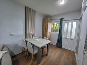 A dining area with a table, chairs, a vase with flowers, a window with curtains, and a door.