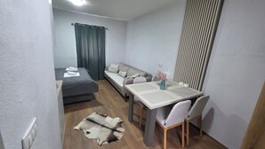 A compact hotel room with a bed, a sofa, a dining table with chairs, a rug, and a decorative vase. - Apartments Javorje- Alpine Atelier Studio (Žabljak)