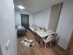 A compact hotel room with a bed, a sofa, a dining table with chairs, a rug, and a decorative vase.