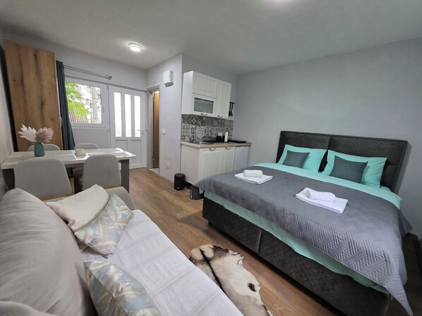 A bedroom with a bed, a small kitchenette, a dining area, and a view of the outdoors.