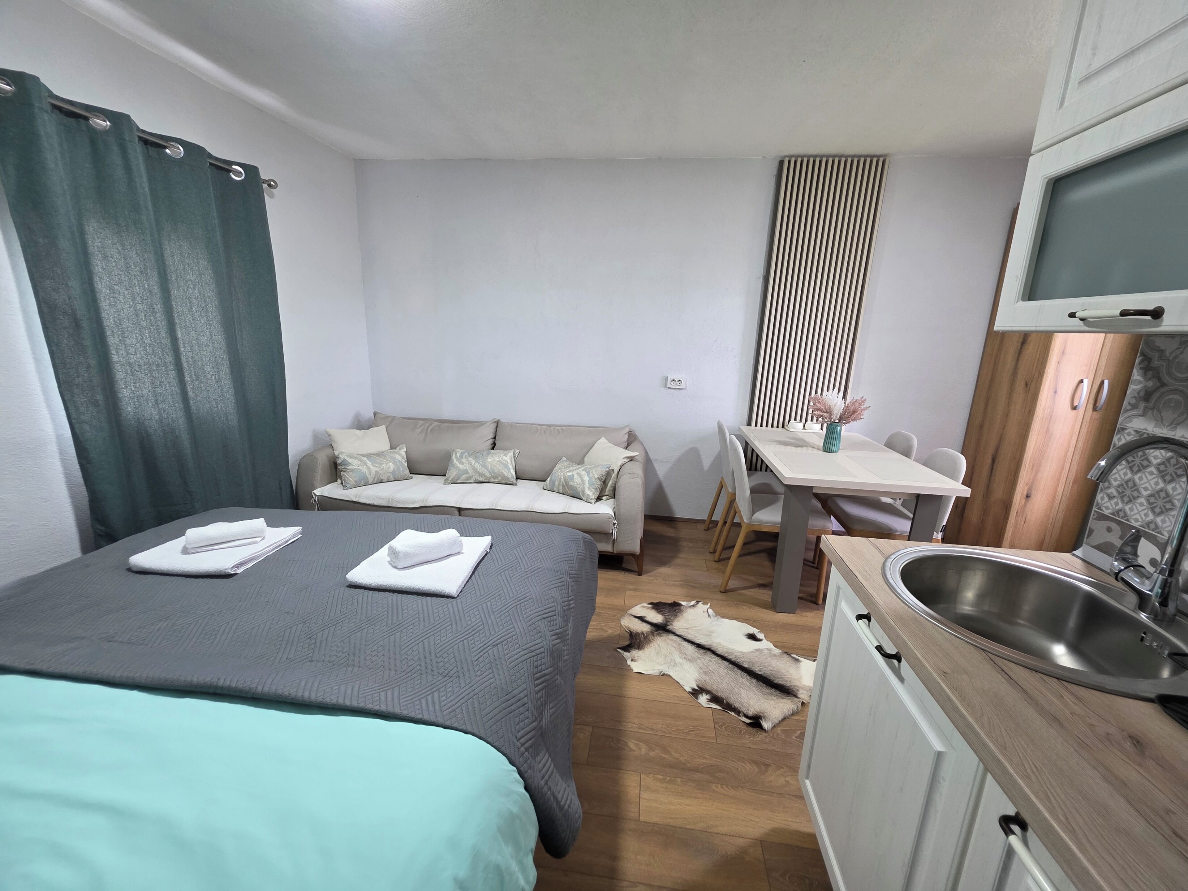 A room with a bed, a sofa, a dining table, and a kitchen area.
