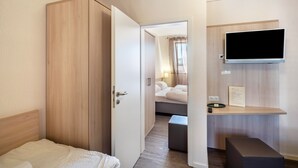 Ett hotellrum med en garderob i trä, en säng, en tv som är monterad på väggen och ett litet bord med en fjärrkontroll.