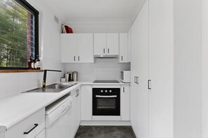 Eine kompakte Küche mit weißen Schränken, einer Edelstahl-Spüle, einer Mikrowelle und einem Backofen.