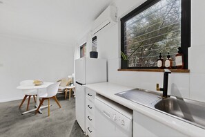 Eine moderne Küche mit weißen Schränken, einer eingebauten Spüle und einem Fenster mit Blick auf einen Baum.