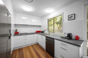 Eine moderne Küche mit weißen Schränken, einem Edelstahl-Kühlschrank, einem Geschirrspüler und einem Fenster mit Jalousien.