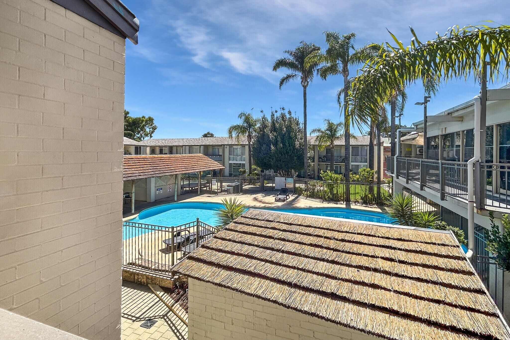 A pool area with a thatched roof, palm trees, and a clear blue sky.
