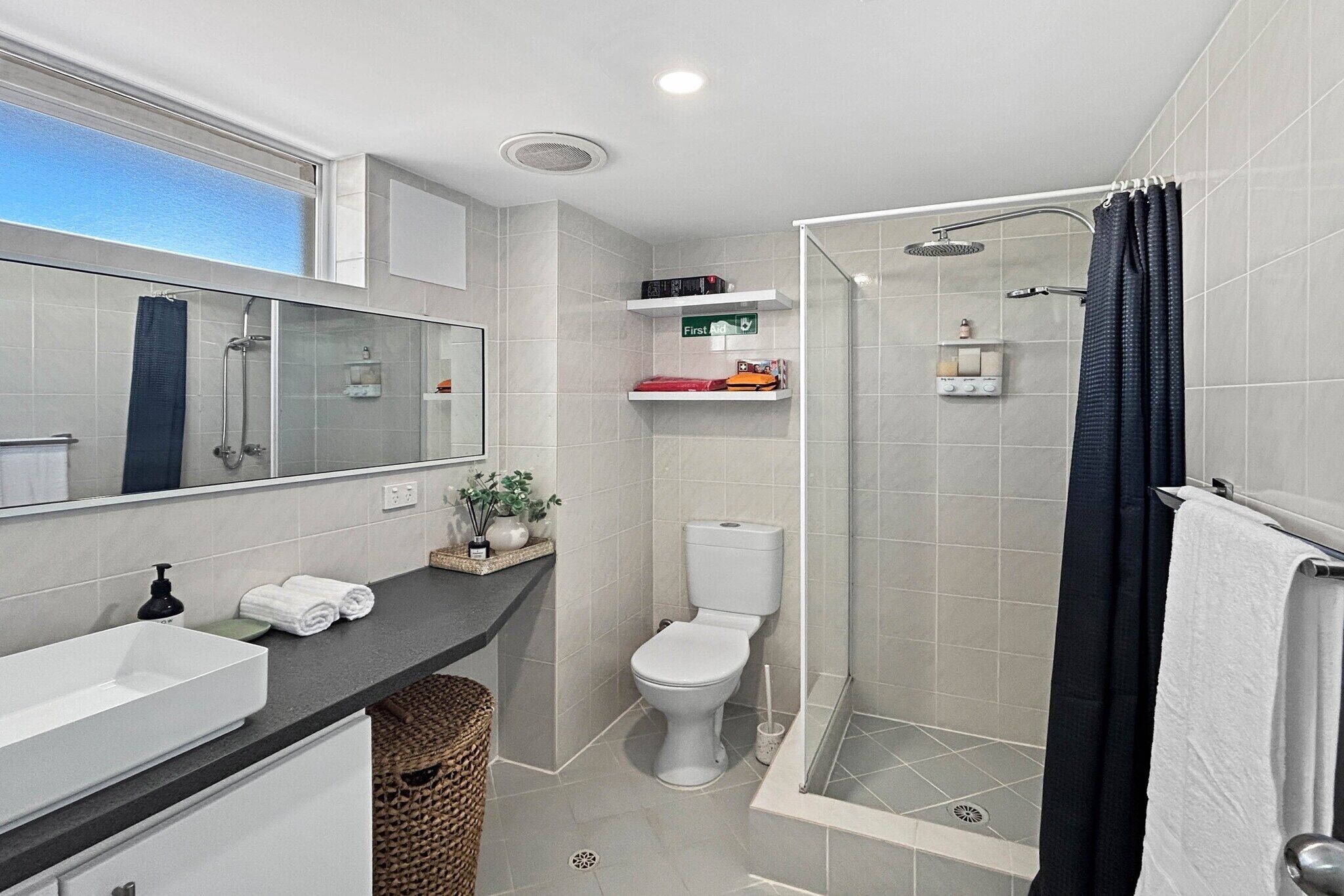 A modern bathroom with a large mirror, a white sink, a toilet, a shower with a glass door, and a towel rack.
