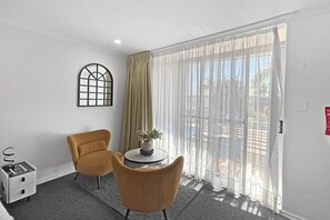 Ein Zimmer mit Bett, Fenster mit Blick, Stuhl, Tisch mit Pflanze und einem kleinen Nachttisch.