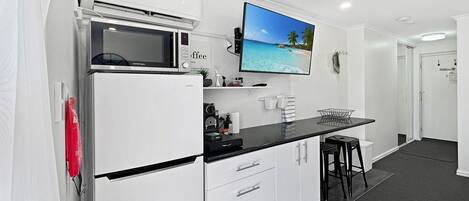 A compact kitchen with a microwave, a coffee machine, a flat-screen TV, and a small bar area with stools.