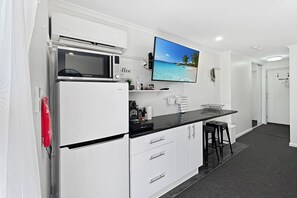 Eine kompakte Küche mit Mikrowelle, Kaffeemaschine, Flachbildfernseher und einer kleinen Bar mit Hockern.