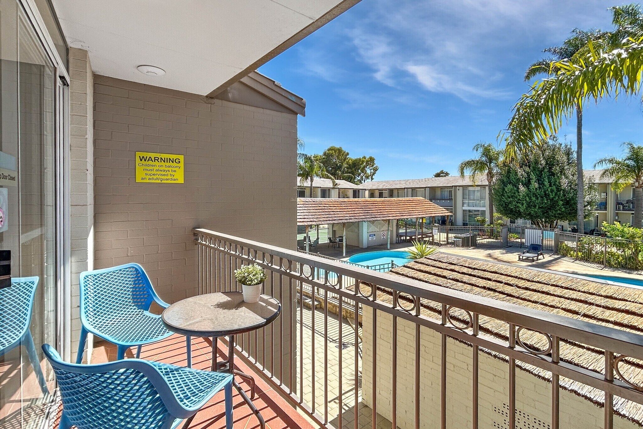 A balcony with blue chairs, a small table, and a warning sign.
