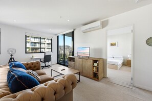 Ein modernes Wohnzimmer mit Sofa, Fernseher und Blick auf einen Balkon.