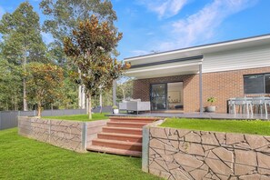 A modern house with a brick exterior, a covered patio with outdoor furniture, and a stone staircase leading to the entrance. - Quiet Retreat with Large Garden and Parking (Malua Bay)