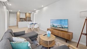 Ein modernes Wohnzimmer mit einer Couch, einem Couchtisch, einem Fernseher und einem Essbereich mit Stühlen und einem Tisch.