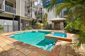 Ein moderner Wohnkomplex mit Schwimmbad, Balkonen und üppiger Bepflanzung.