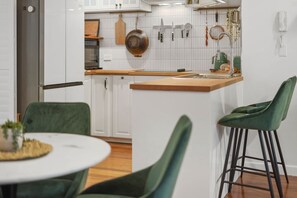 Eine moderne Küche mit weißen Schränken, einer Holzausziehtheke und grünen Stühlen.