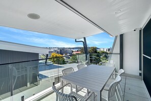 Een balkon met glazen hekwerk, een tafel en stoelen.