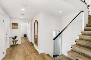 Een trap met houten treden en een glazen balustrade, een hal met houten vloer en een grote spiegel aan de wand.