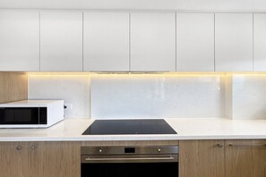 Een moderne keuken met witte kasten, een ingebouwde magnetron, een zwart inductiefornuis en een roestvrijstalen oven.