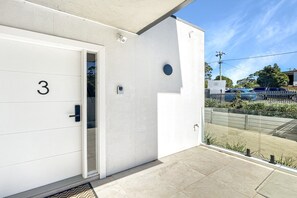 Een modern gebouw met een witte gevel, een deur met nummer en een glazen ingang.