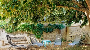 Ein Garten mit Steinmauer, einer Holzbank und Metallstühlen unter einem Baum.