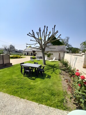 A well-maintained garden with a dining table and chairs, a tree, and a flower bed.