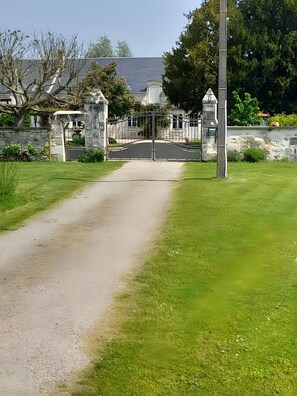 A paved path leading to a gated entrance with a stone wall and a building in the background.