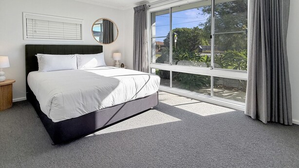Quarto moderno com uma cama grande, um ventilador de teto, uma janela com cortinas e vista para o verde lá fora.