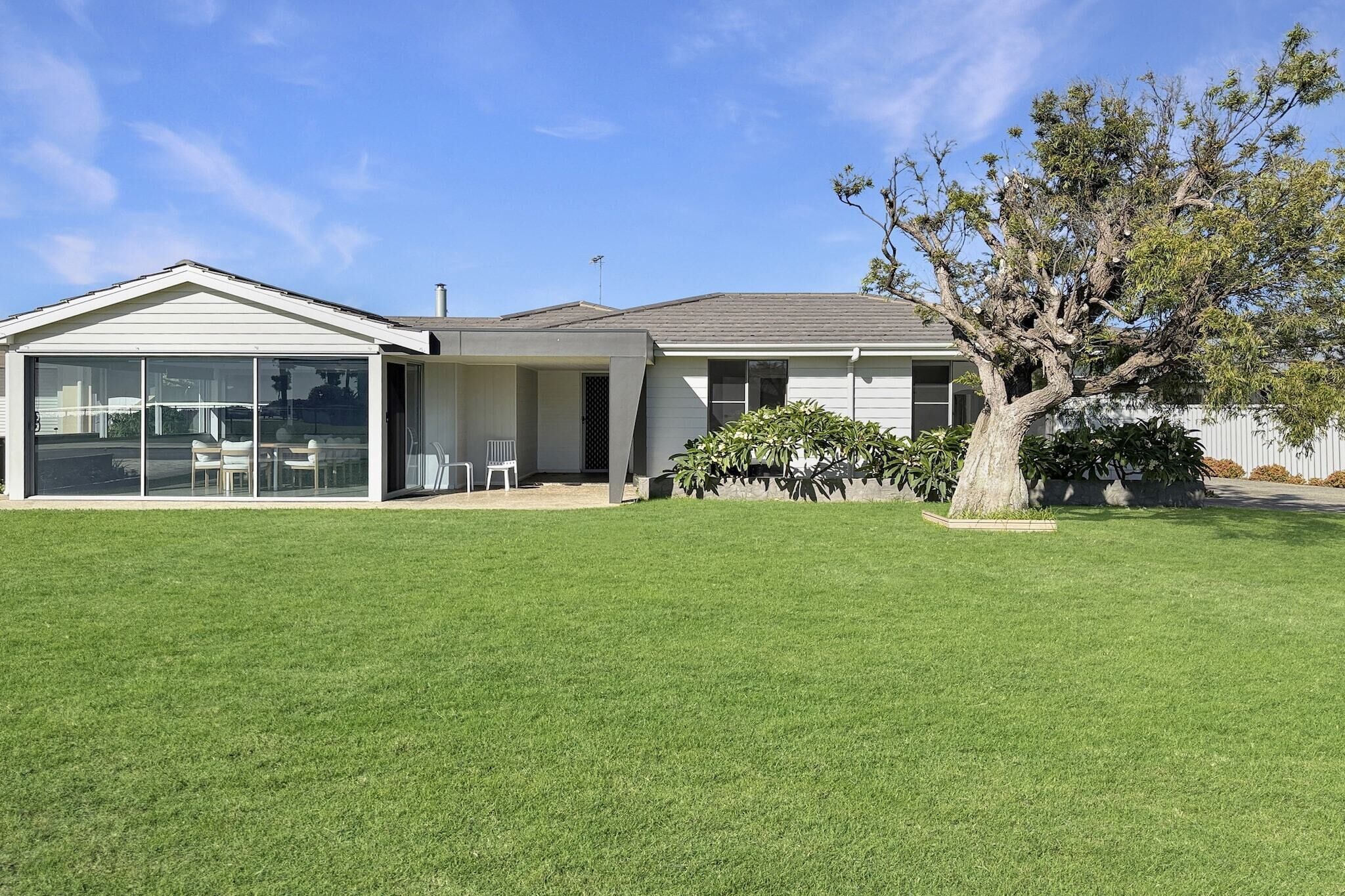 A single-story house with a large glass sliding door, a covered patio, and a well-maintained lawn.