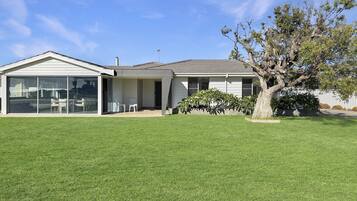 A single-story house with a large glass sliding door, a covered patio, and a well-maintained lawn.