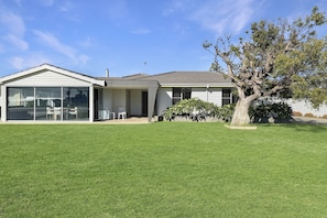 A single-story house with a large glass sliding door, a covered patio, and a well-maintained lawn. - Comfortable Stay Near Busselton Beach (West Busselton)