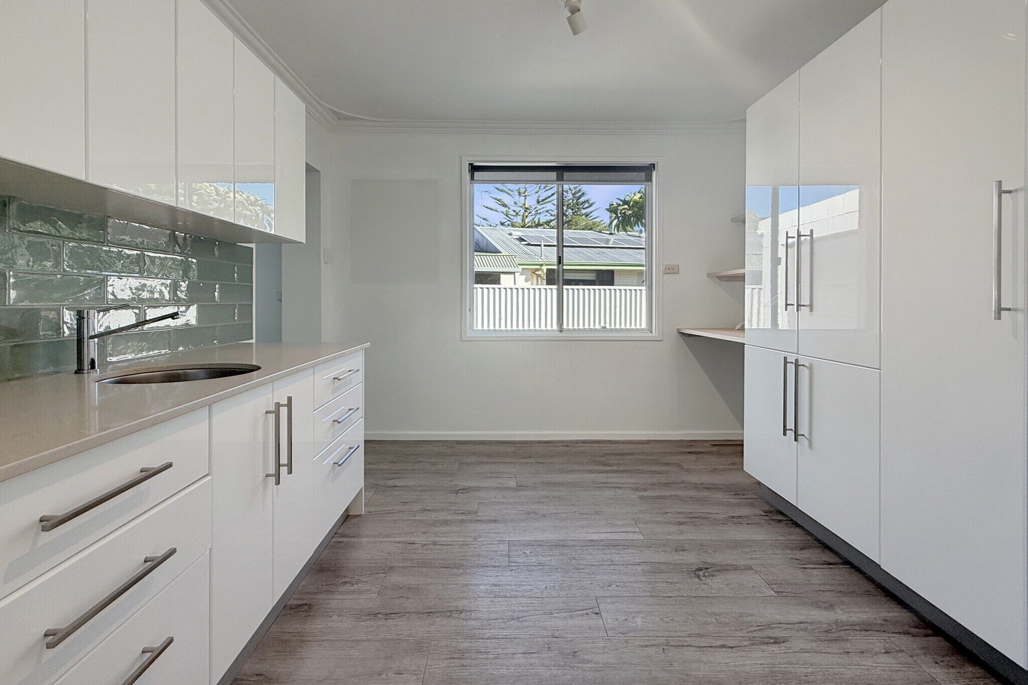 A modern kitchen with white cabinets, a large window, and a view of a house.