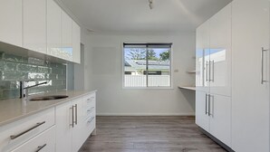 Cozinha moderna com armários brancos, uma janela ampla e vista para uma casa.