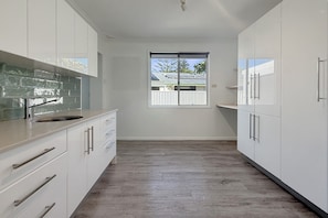 A modern kitchen with white cabinets, a large window, and a view of a house. - Comfortable Stay Near Busselton Beach (West Busselton)