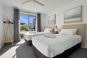 Habitación de hotel con dos camas, ventilador de techo, ventana con cortinas y cuadros en las paredes.