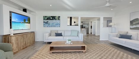 A modern living room with a flat-screen TV, two white sofas, a wooden coffee table, and a patterned rug.