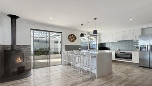 Uma cozinha moderna com uma ilha central, banquetas, fogão embutido e uma grande porta de vidro que dá para uma área externa.