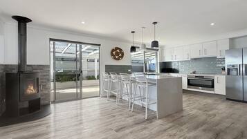 A modern kitchen with a central island, bar stools, a built-in stove, and a large glass door leading to an outdoor area.