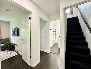 A hallway with a staircase, a door leading to a bathroom, and a television mounted on the wall.