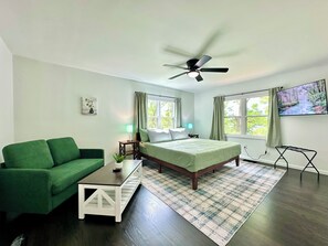 A bedroom with a bed, a green couch, a small table, a ceiling fan, two bedside lamps, a TV, and a window with curtains. - BRAND NEW! 10 Min To Hershey w/ Firepit & Gameroom (Hummelstown)