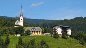 A rural church with a tall steeple, a yellow building, and a white building with balconies.