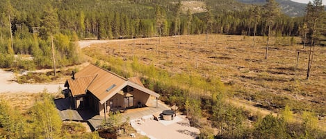 A cabin with a sloped roof, surrounded by a forested area with a dirt path leading to it.