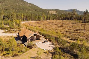 A cabin with a sloped roof, surrounded by a forested area with a dirt path leading to it.