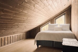 Een slaapkamer met een schuine kap, een bed met witte beddengoed, en een raam.