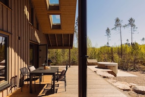 A wooden deck with a table and chairs, a hot tub, and a view of trees.