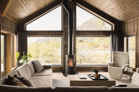 A cozy room with a fireplace, large windows, a sofa, and a chair.. Det Kosekroken with jacuzzi