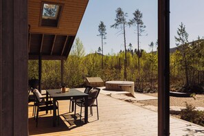 A wooden deck with a table and chairs, a hot tub, and a view of a forested area.