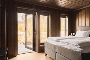 Ein Schlafzimmer mit einem Bett, einem Nachttisch und einem Fenster mit Blick auf Bäume.